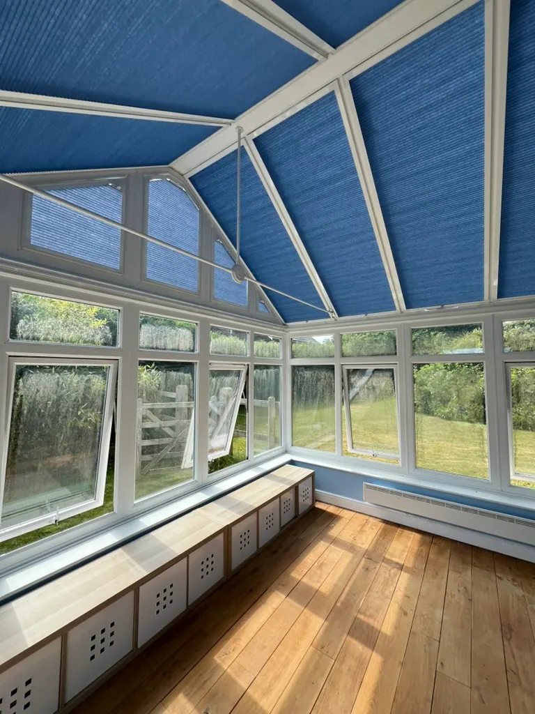 Blue pleated blinds fitted across a white-framed glass conservatory roof