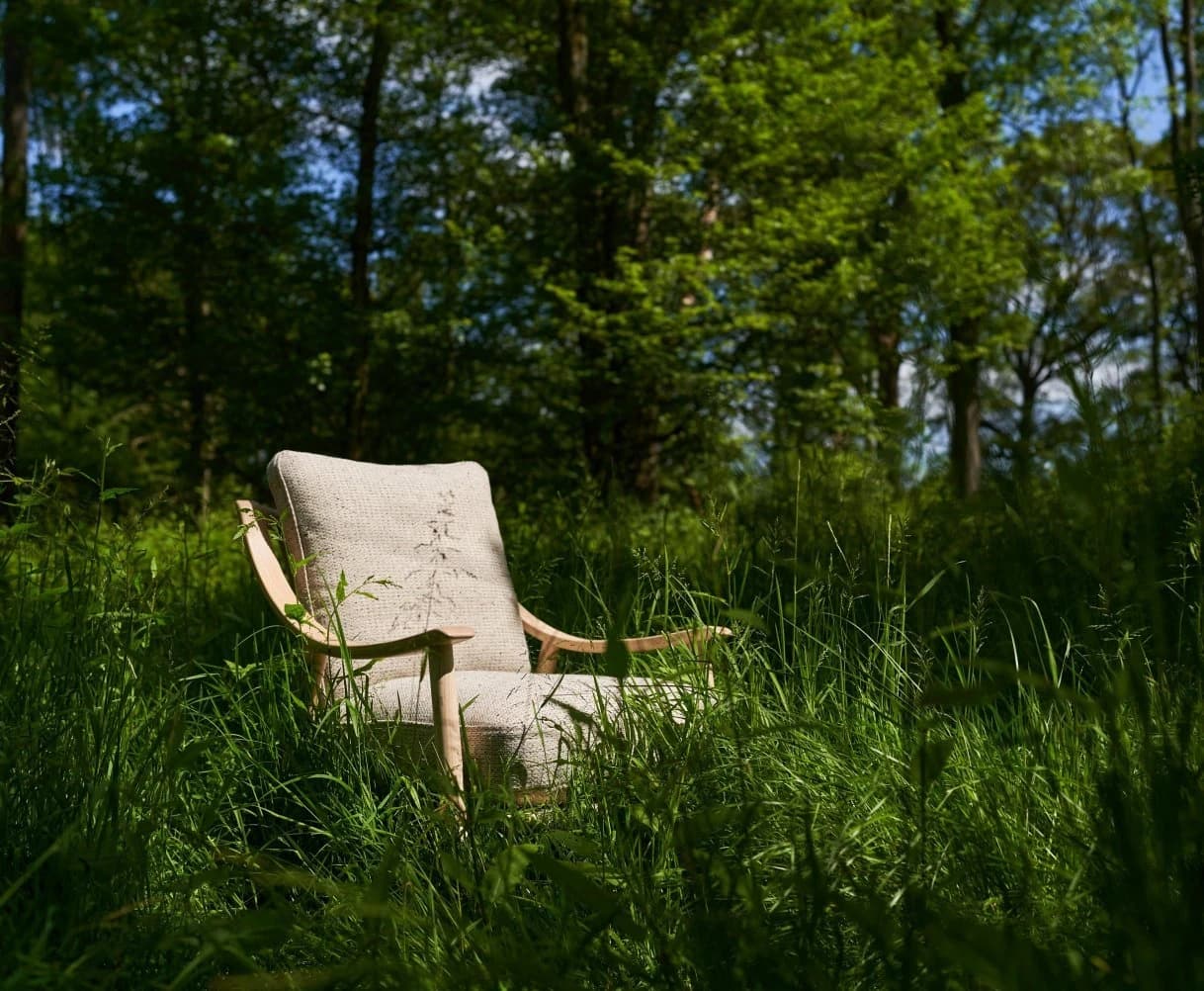 Ercol wooden chair standing in long grass outdoors, showing natural ash grain and steam-bent form