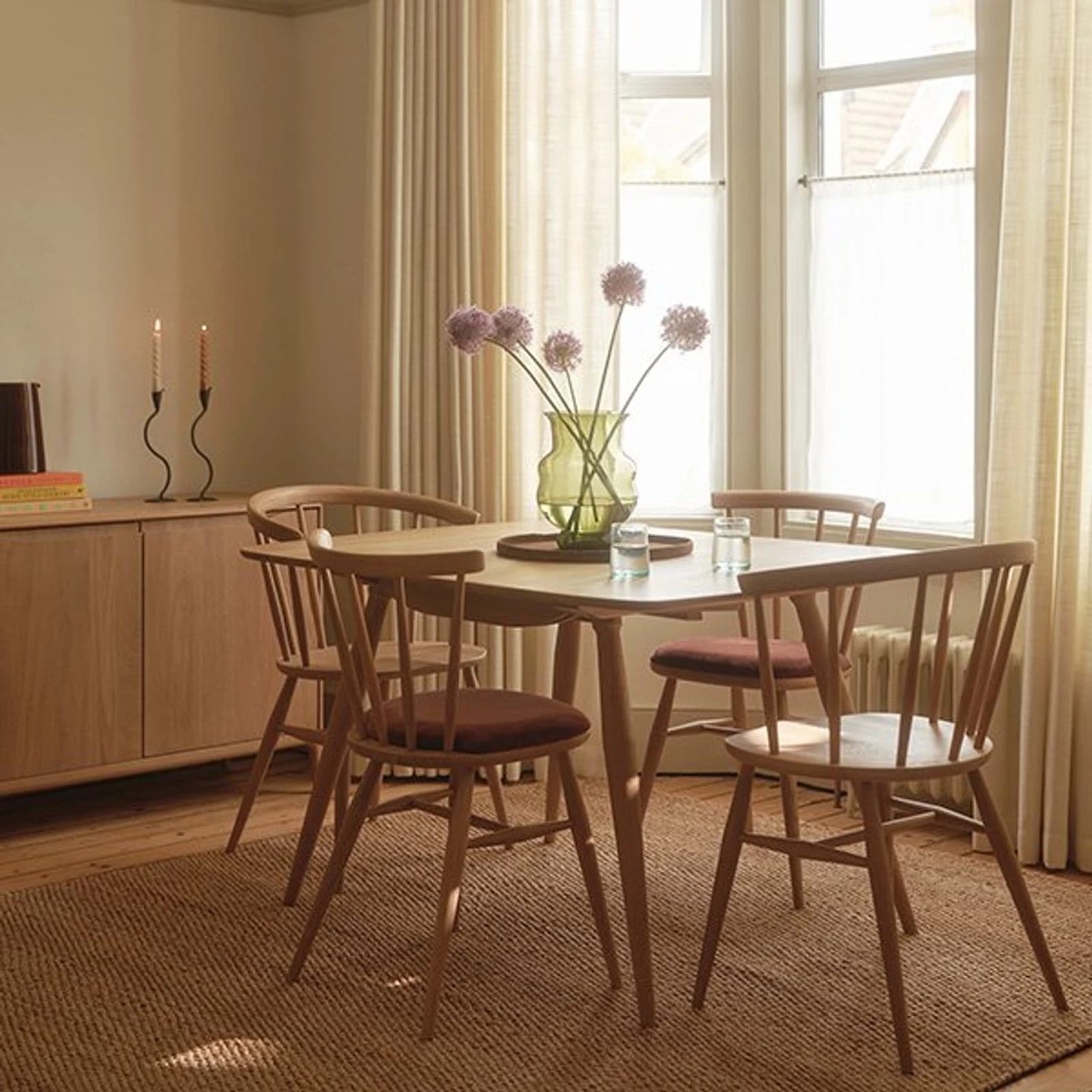 Ercol light wood dining table with spindle-back chairs and matching sideboard in a sunlit dining room