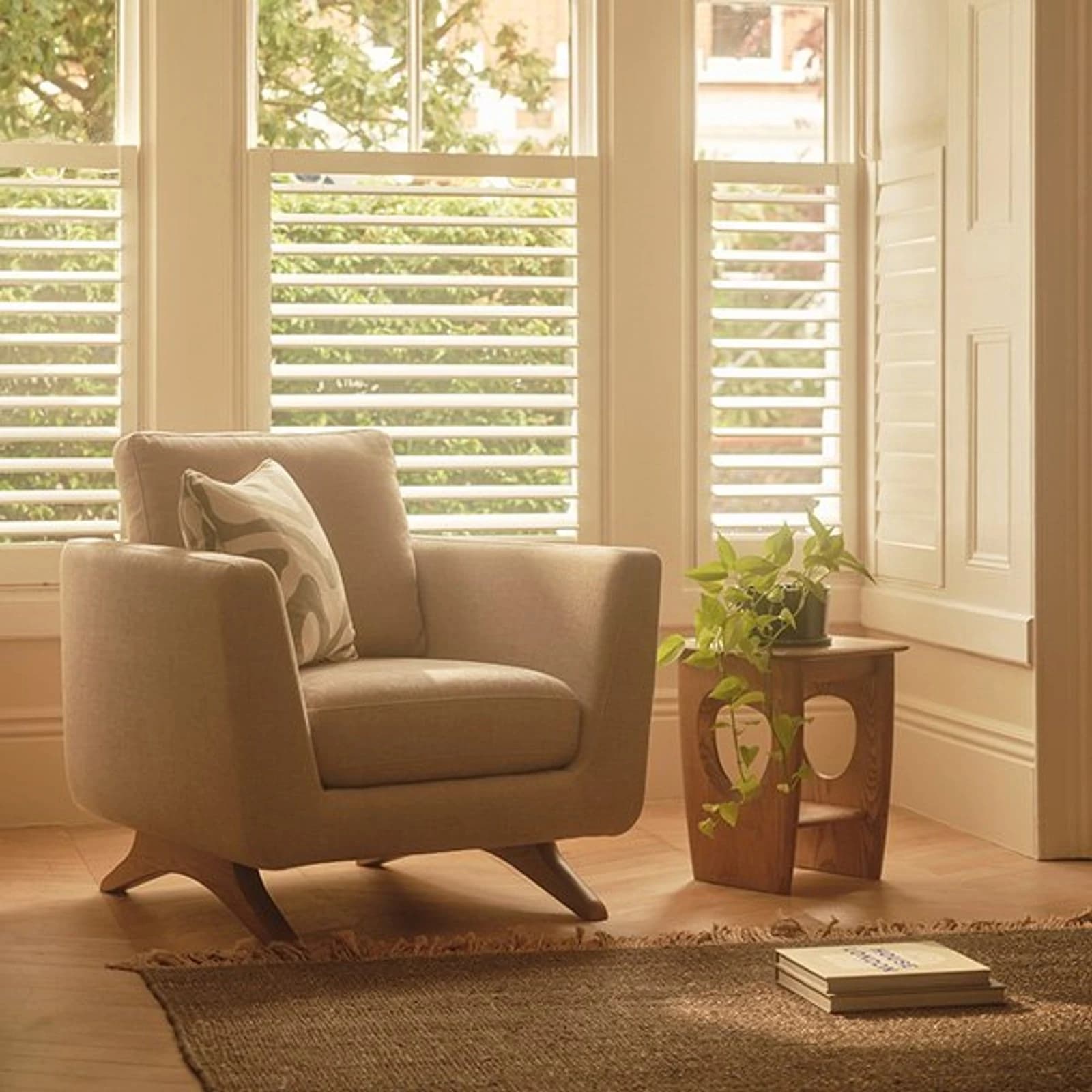 Ercol upholstered armchair and wooden side table with circular cutouts beside window shutters