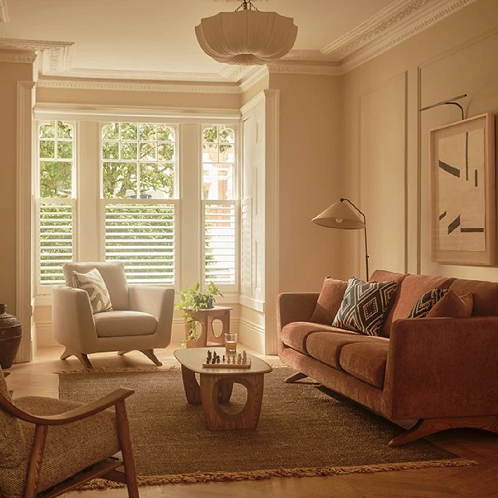 Ercol terracotta sofa and oval wooden coffee table in a living room with plantation shutters