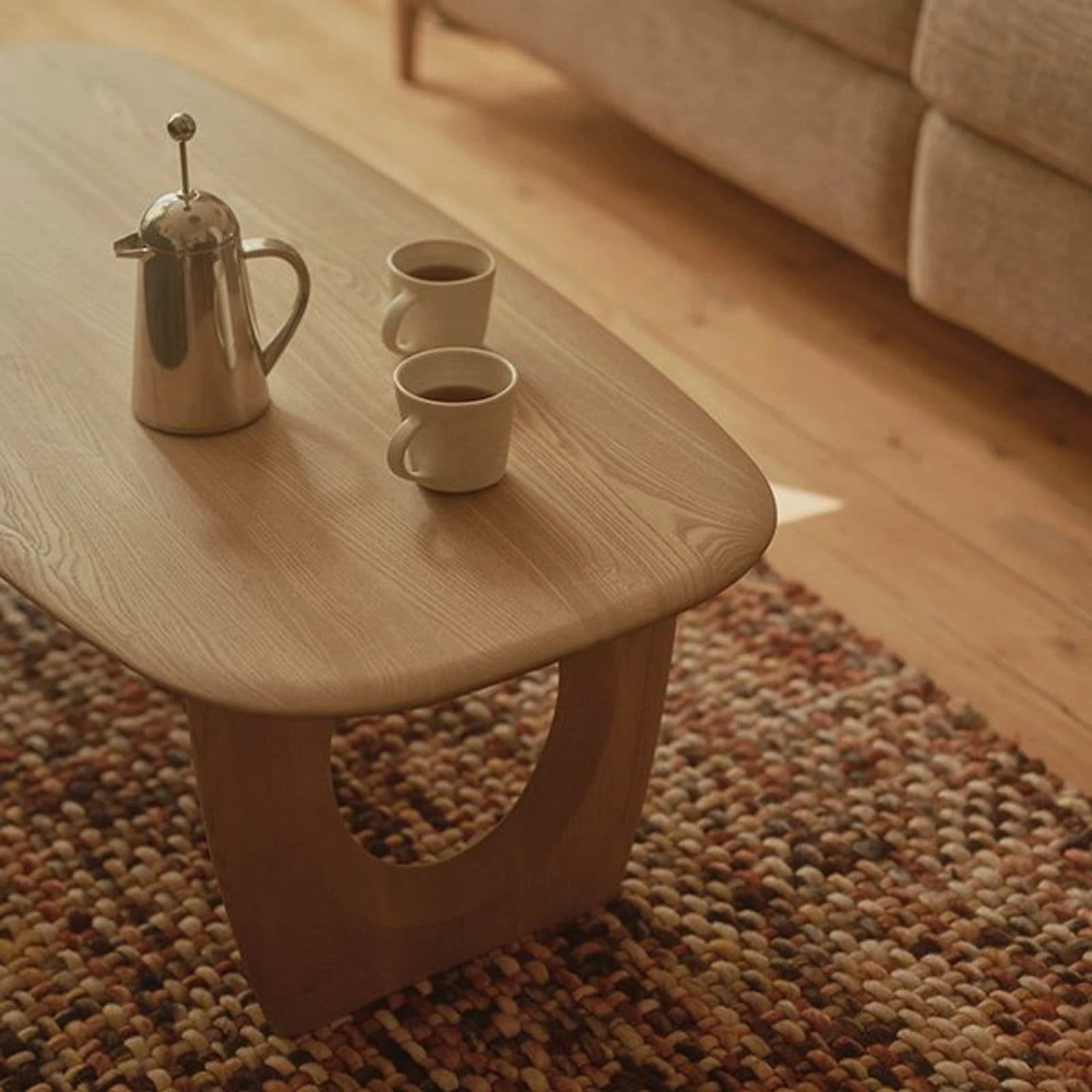 Ercol light wood oval coffee table with circular cutout base, coffee cups and cafetière on a textured rug