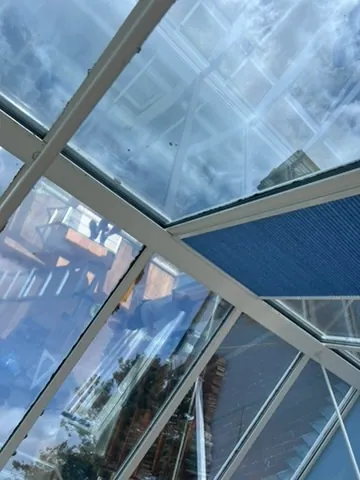Looking up at blue pleated conservatory roof blinds against a bright sky