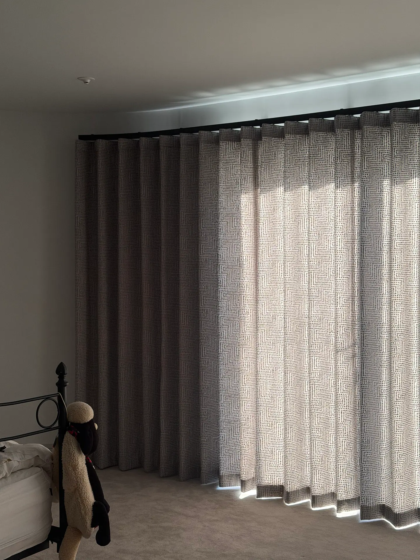 Floor-length layered curtains on a curved bedroom track, patterned sheer over a solid lining