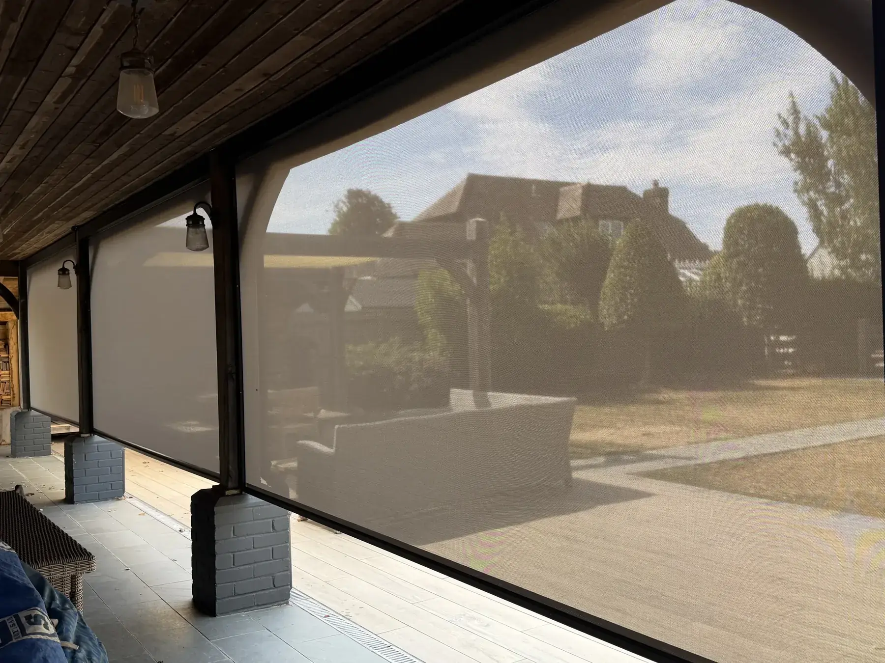 Wide view through three Luxaflex external screen blinds across a patio opening to landscaped garden