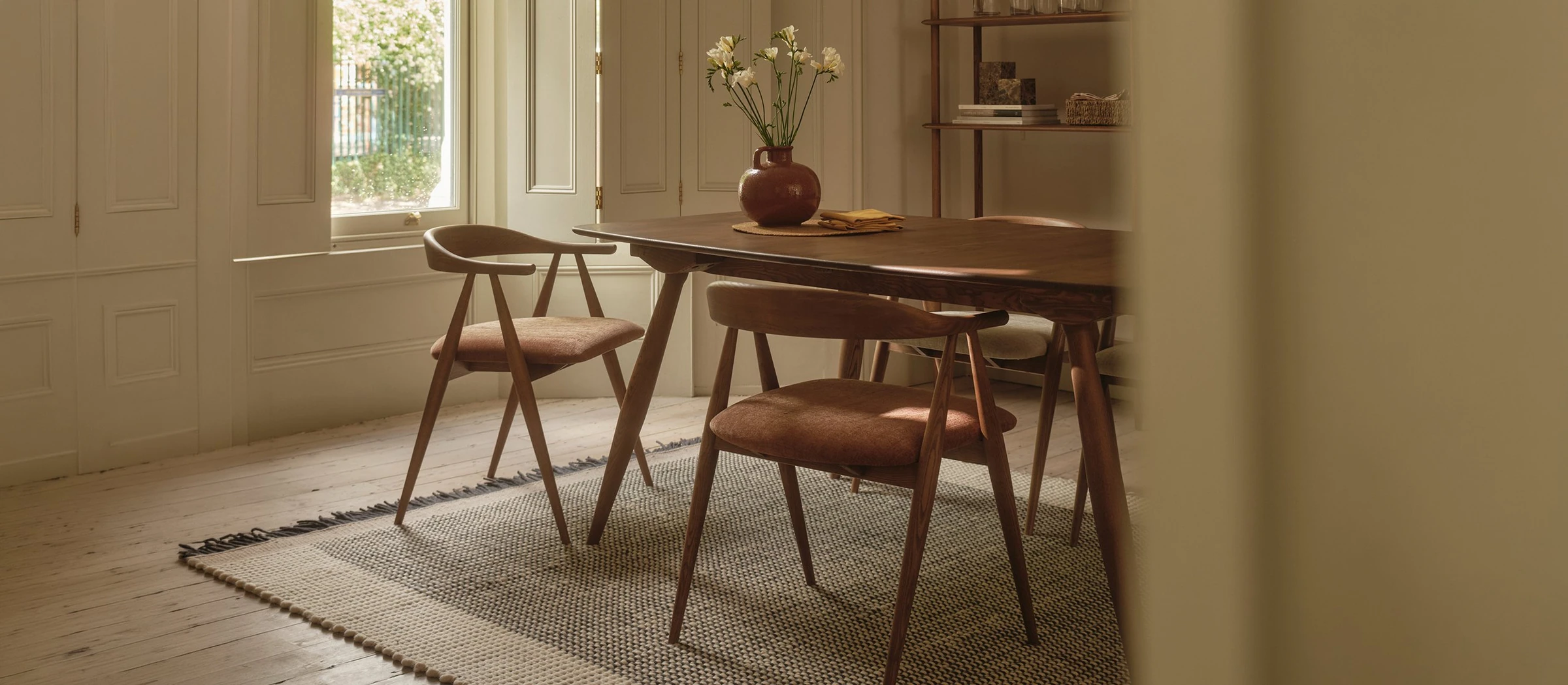 Ercol dark wood dining table with terracotta upholstered chairs in a bright room with shutters