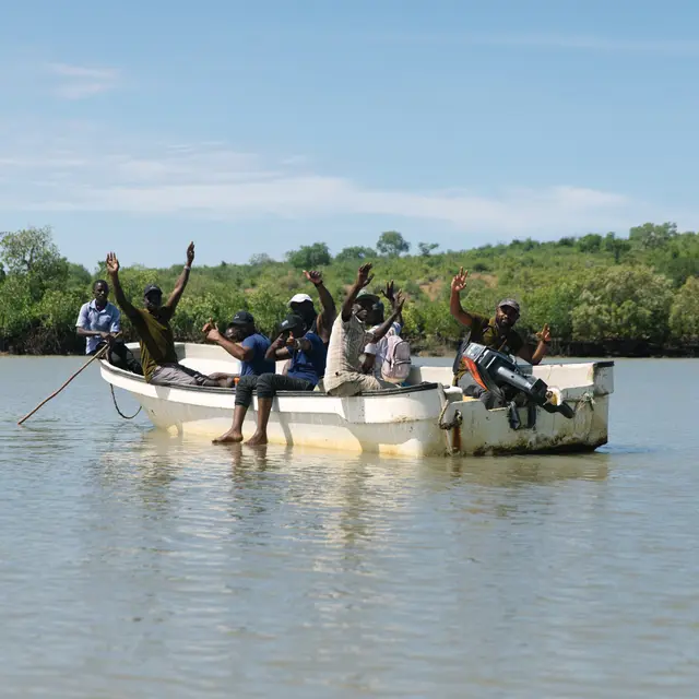 A planting team waving from a small boat along a green shoreline