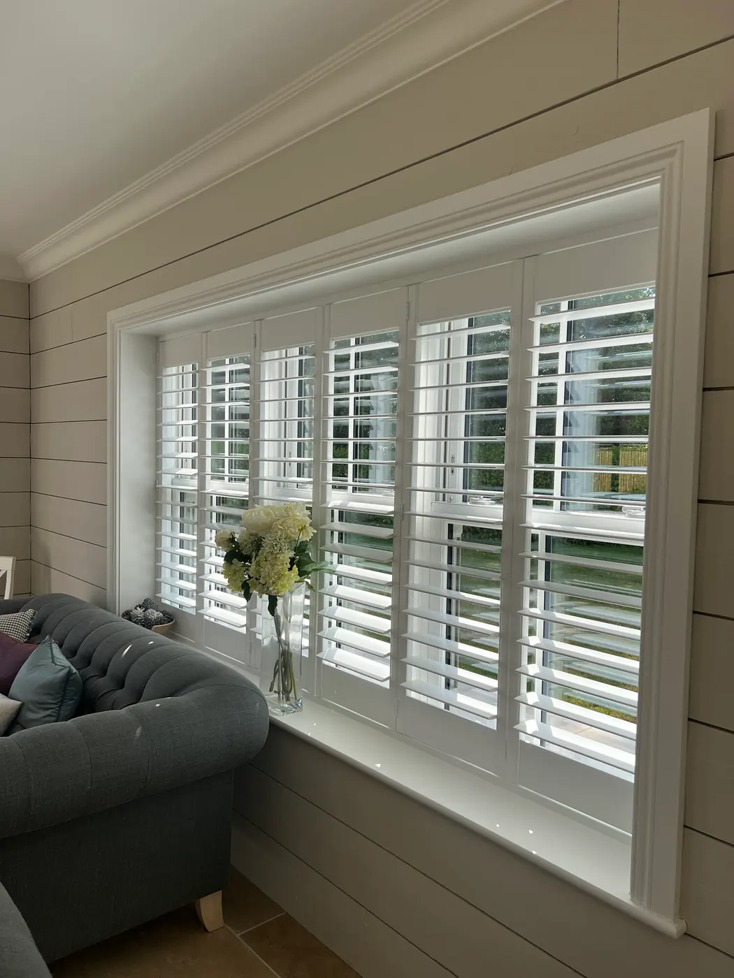 Full-height white shutters on a wide living-room window with open louvres, measured and fitted in Hampshire