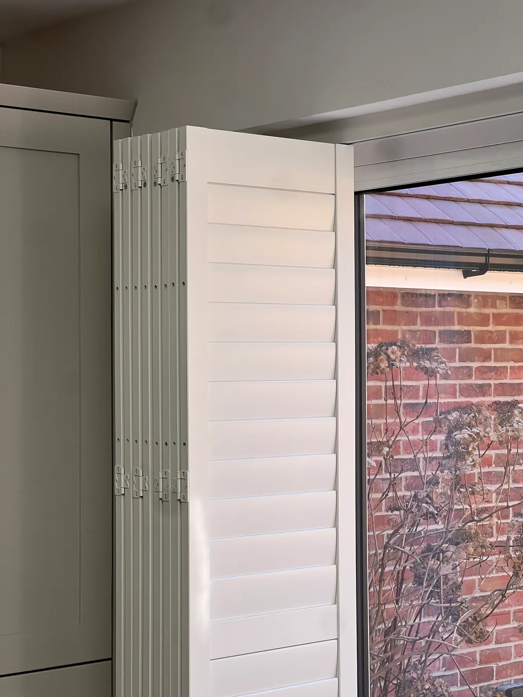 Tracked white bi-fold shutters stacked beside a patio door for wide openings, Crestwood of Lymington