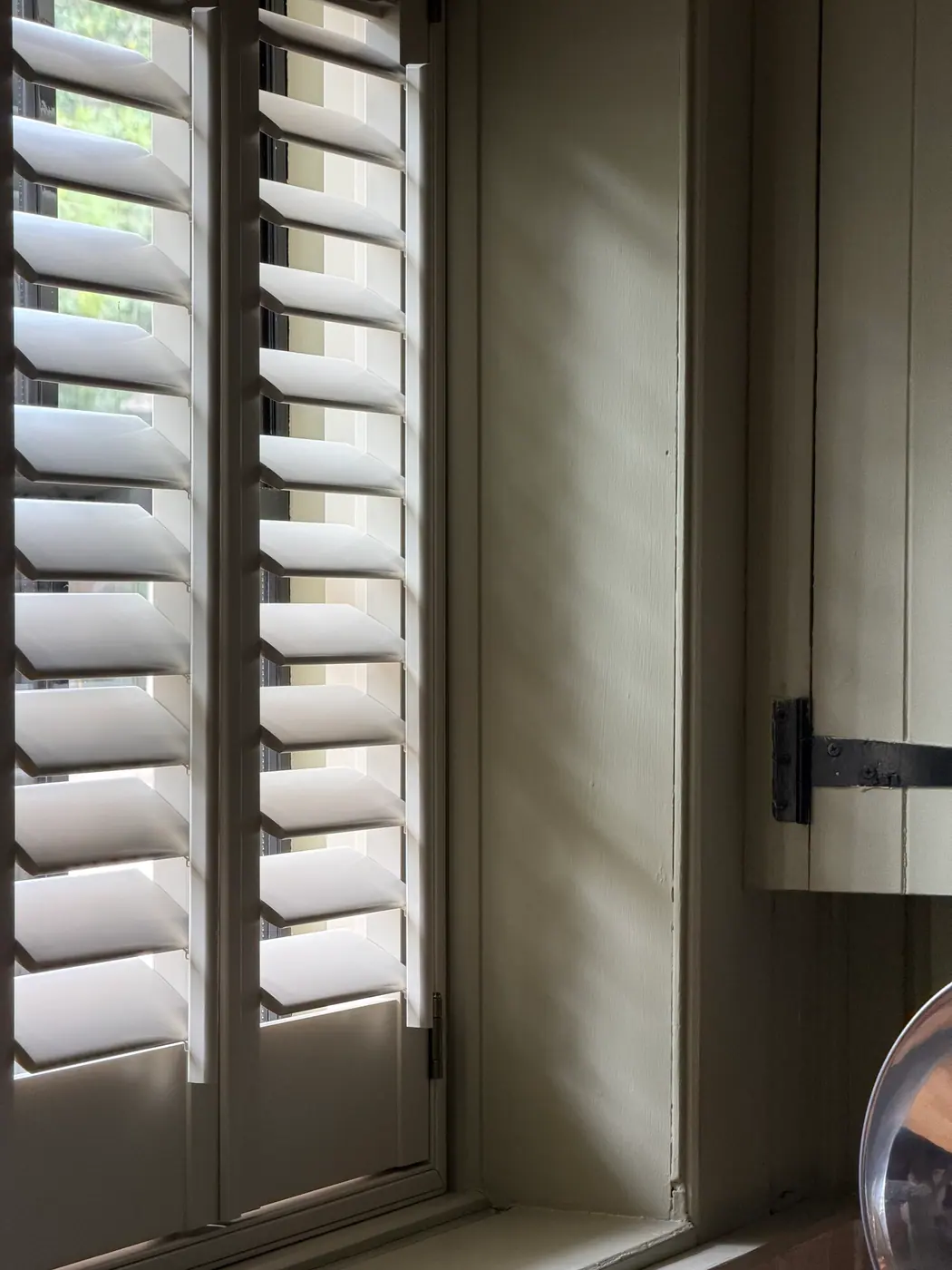 Half-height white interior shutters with louvres tilted for street privacy and soft daylight, Lymington showroom range
