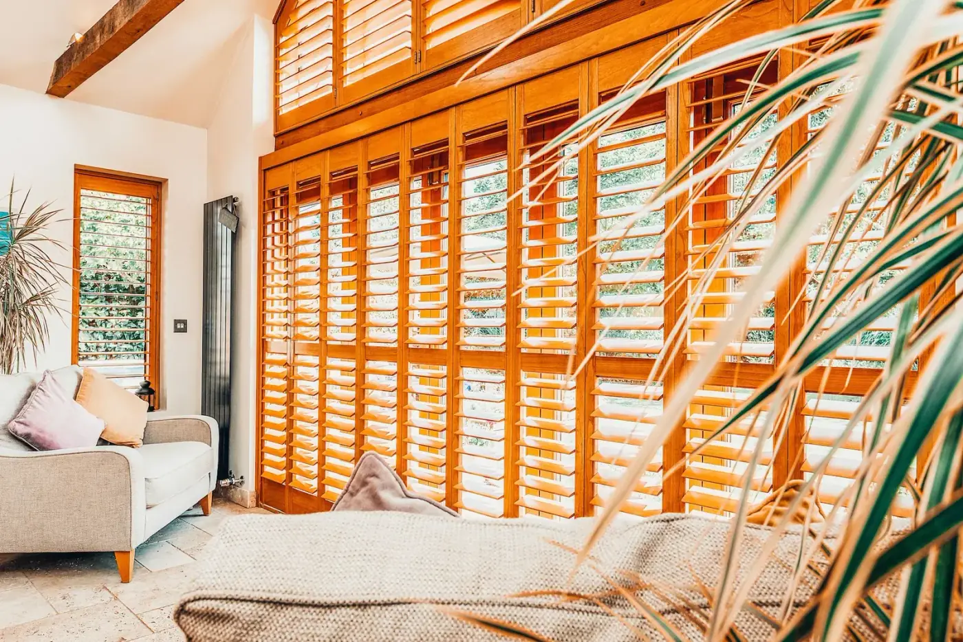 Warm timber interior shutters across a sunlit living room with a custom arched opening, Crestwood of Lymington