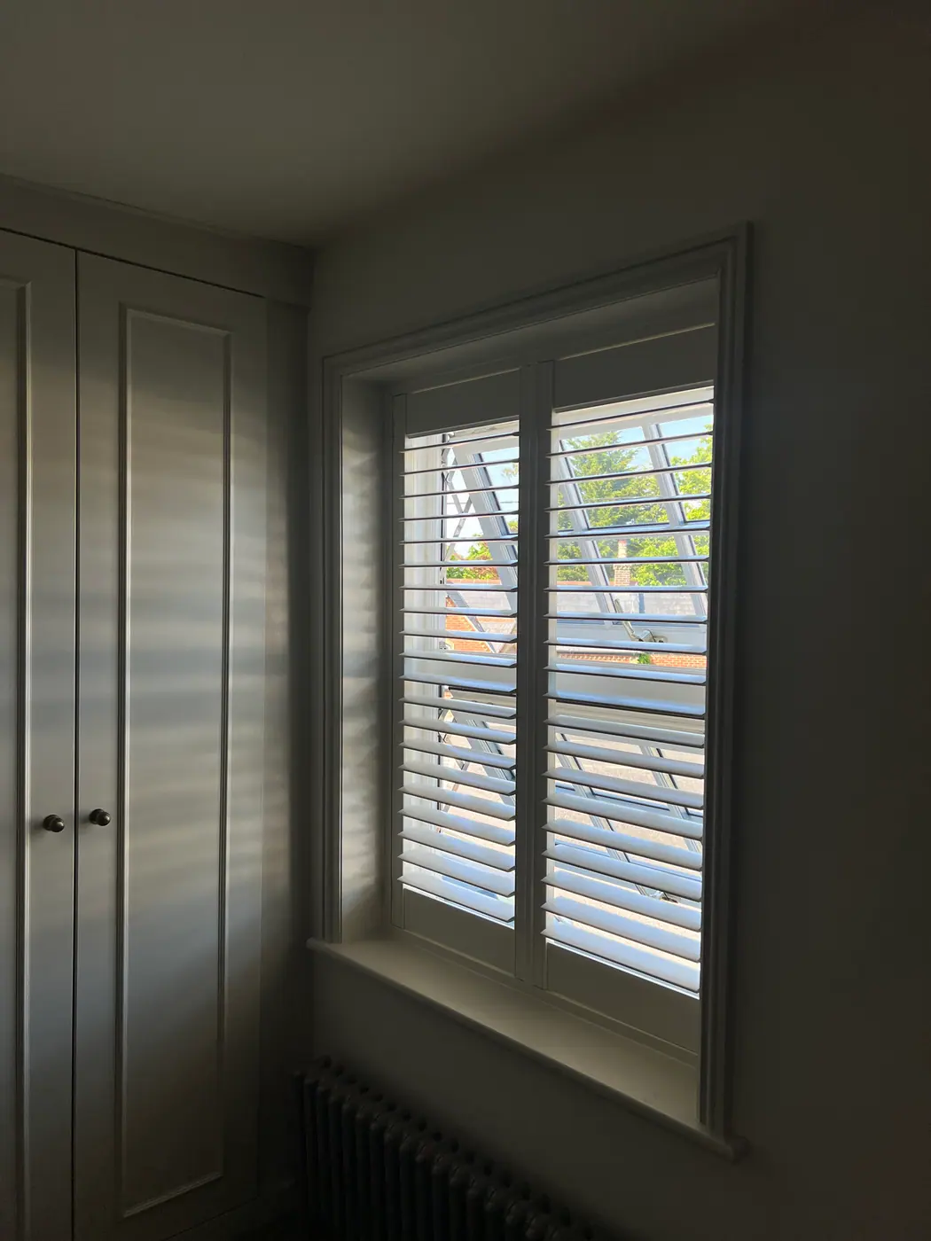 Tier-on-tier white shutters casting linear daylight shadows beside fitted wardrobes in a Hampshire home